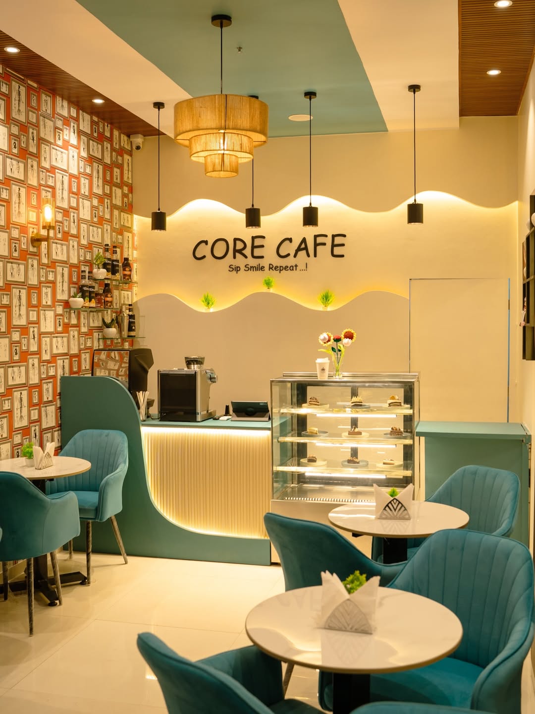 Small cafe with teal velvet chairs, a wavy cream wall and a cake display case