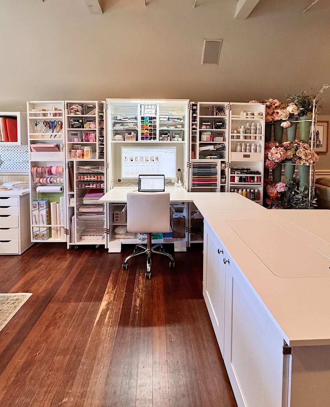 Built-in white cabinet wall with a central desk and computer for a craft room