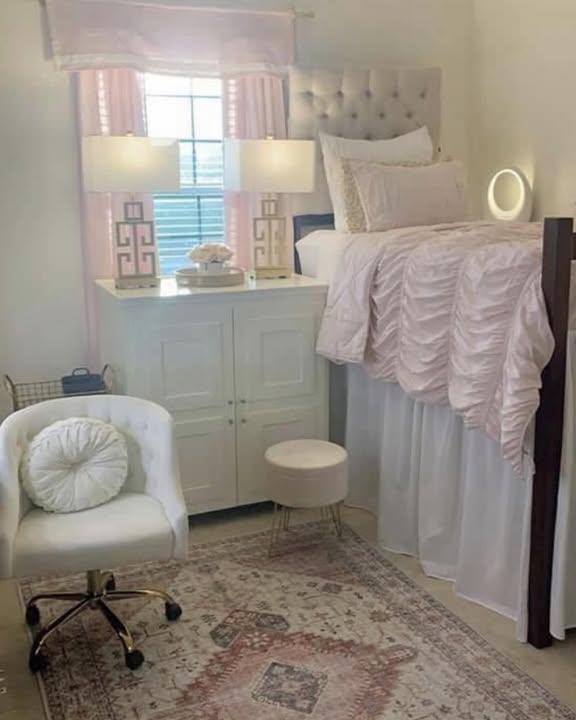Lofted dorm bed with white ruffle bedding, pink Greek key lamps, and a vintage rug