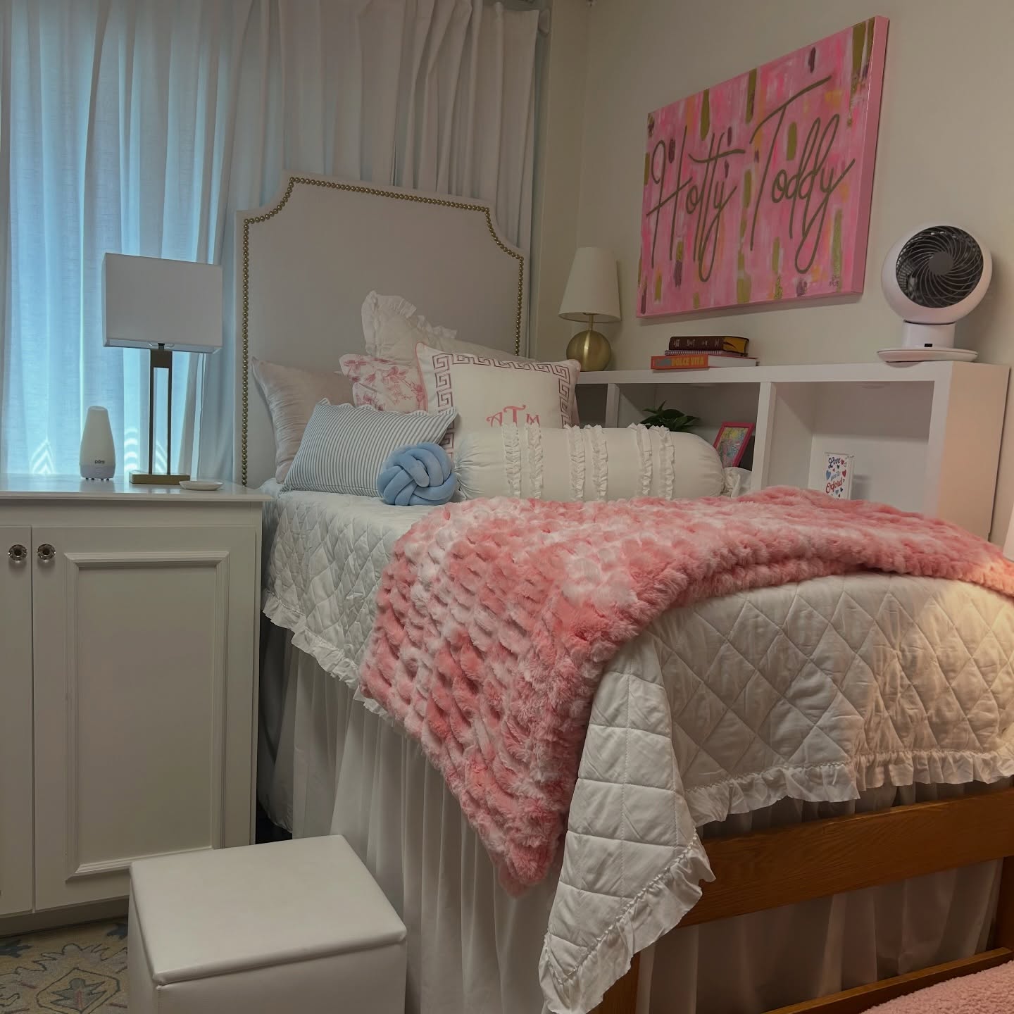 White ruffled dorm bedding layered with a pink faux fur throw and monogram pillow