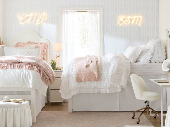 Two white ruffle dorm beds under glowing neon name signs and pale blue wallpaper
