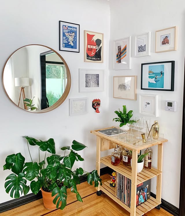 Round wood mirror and colourful framed posters around a corner above a bar cart