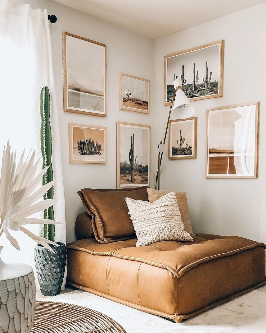 Desert and cactus prints in light oak frames wrapping a corner above a tan leather lounger