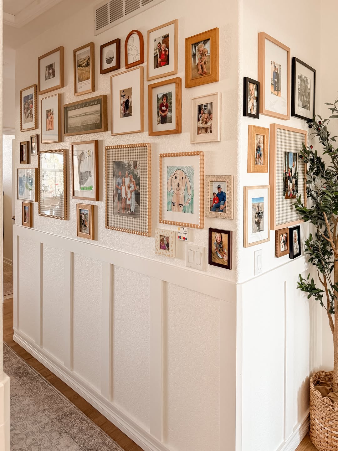 Family photos in wood frames above white board and batten panelling turning a hallway corner